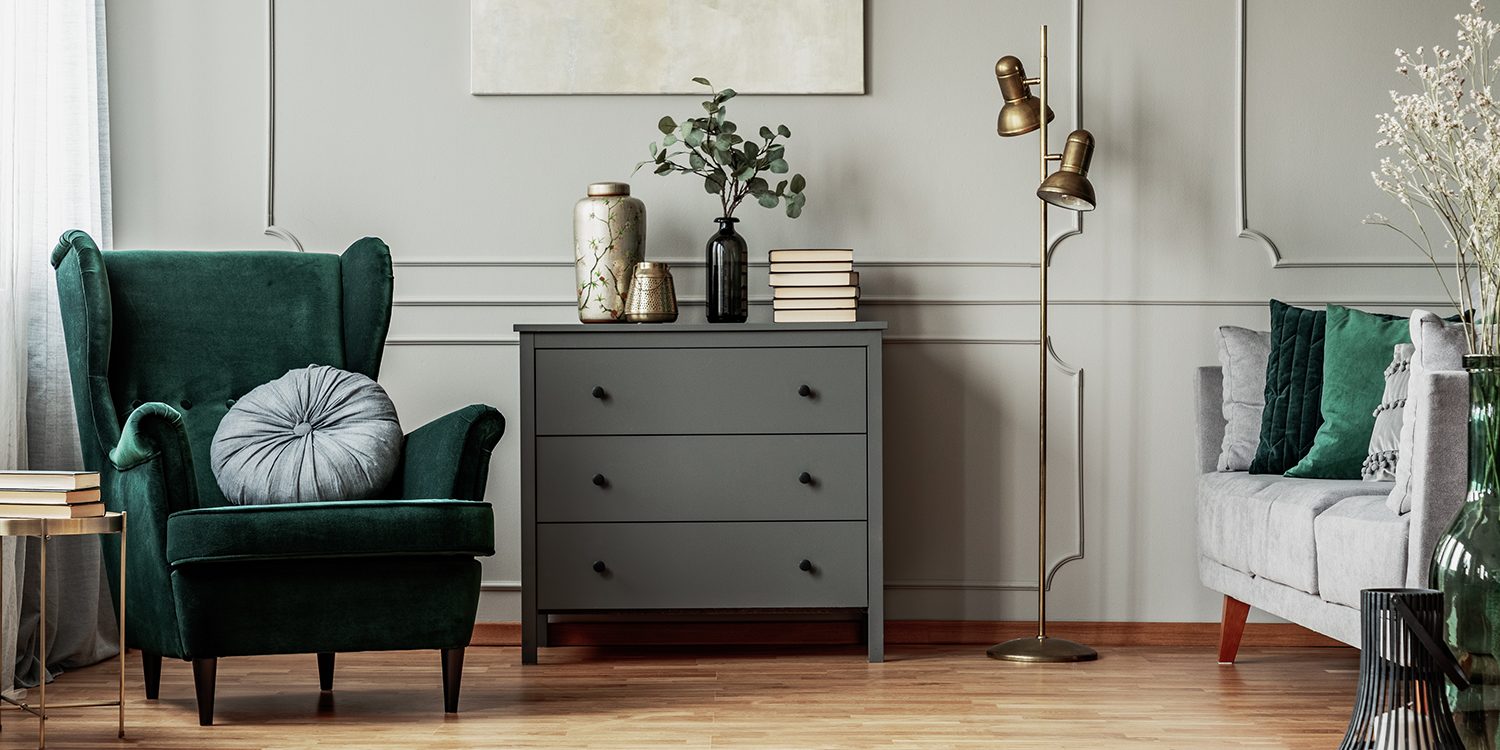 Abstract painting on grey wall o contemporary living room interior with emerald green armchair with round pillow, commode and couch